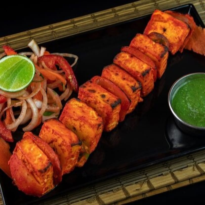 Indian paneer tikka skewers with green chutney and a side salad on a black plate.