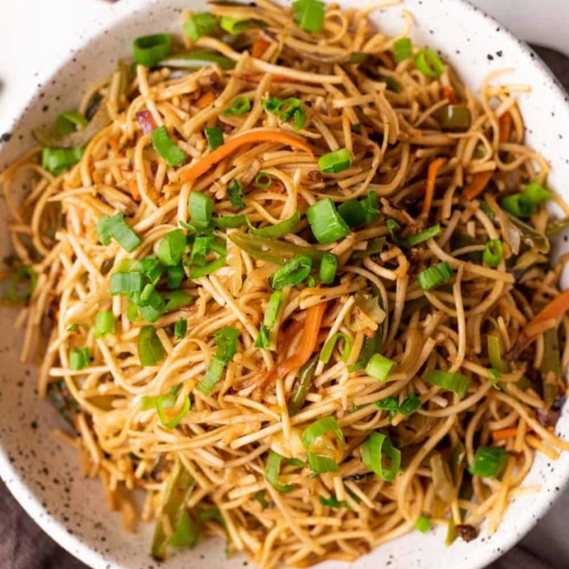 Close-up of Desi Chowk's Indian noodles with vegetables and green onions in a white bowl.