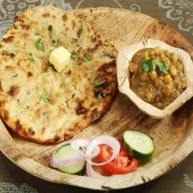 Indian naan bread with butter, chickpea curry, and a side of sliced cucumbers, tomatoes, and onions.