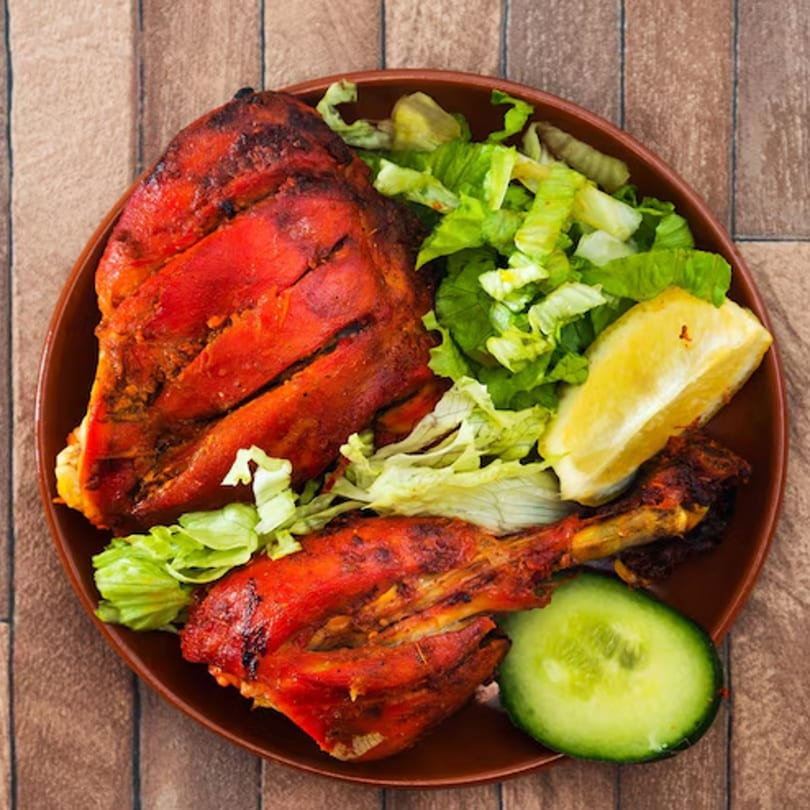 Tandoori chicken with fresh lettuce, a lemon wedge, and cucumber on a brown plate.
